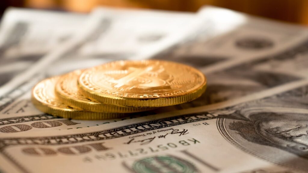 Três moedas redondas de cor dourada em notas de 100 dólares americanos - Freebitcoin