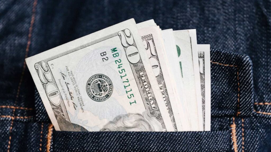 Notas de 20 e 50 dólares no bolso de uma calça - Meta Dólar