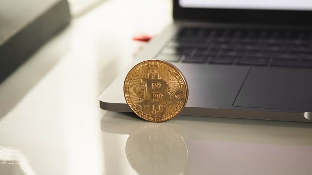Uma moeda de bitcoin ao lado de um notebook